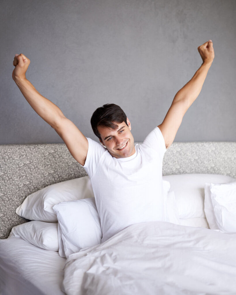 A man stretching happily in bed, representing the positive impact of improved sleep habits from The Comprehensive Sleep Hack.